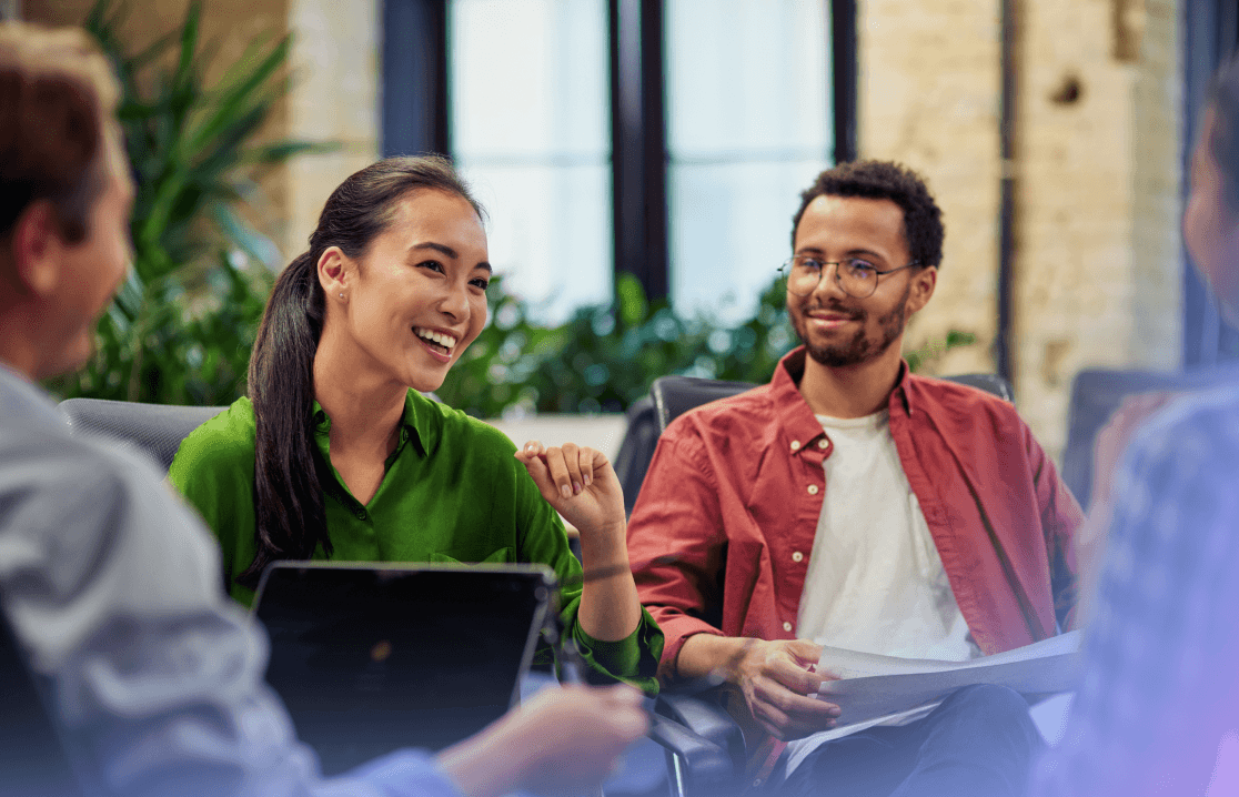 Diverse colleagues smiling and discussing documents together in a modern office meeting.